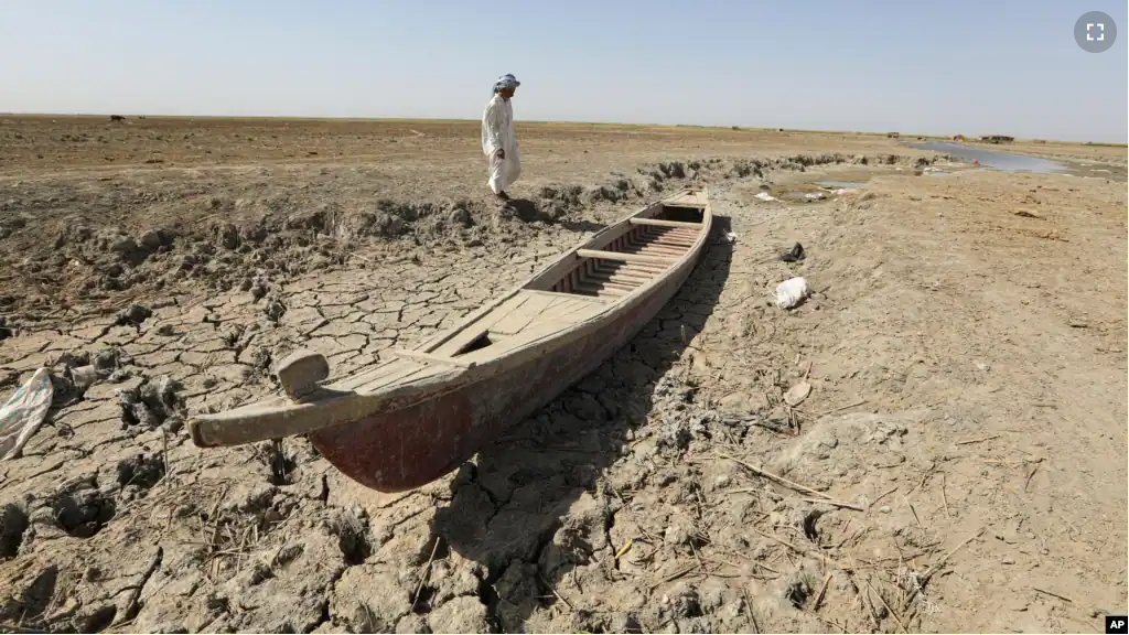 A fisherman stands next to his boat in a dry ground in the Chibaish marshes during low water levels in Nasiriyah of southern Iraq on June 16, 2022. (AP Photo/ Nabil al-Jurani)