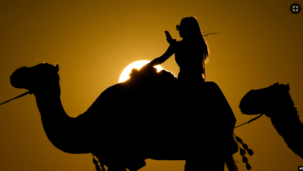 A woman looks at her photo while riding a camel in Mesaieed, Qatar, Nov. 26, 2022. (AP Photo/Ashley Landis)