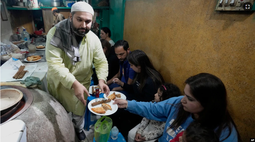 Bilal Sufi, left, owner of Baking Virsa eatery, serves traditional kebabs and naan bread in Lahore, Pakistan, Saturday, Dec. 3, 2022. (AP Photo/K. M. Chaudary)