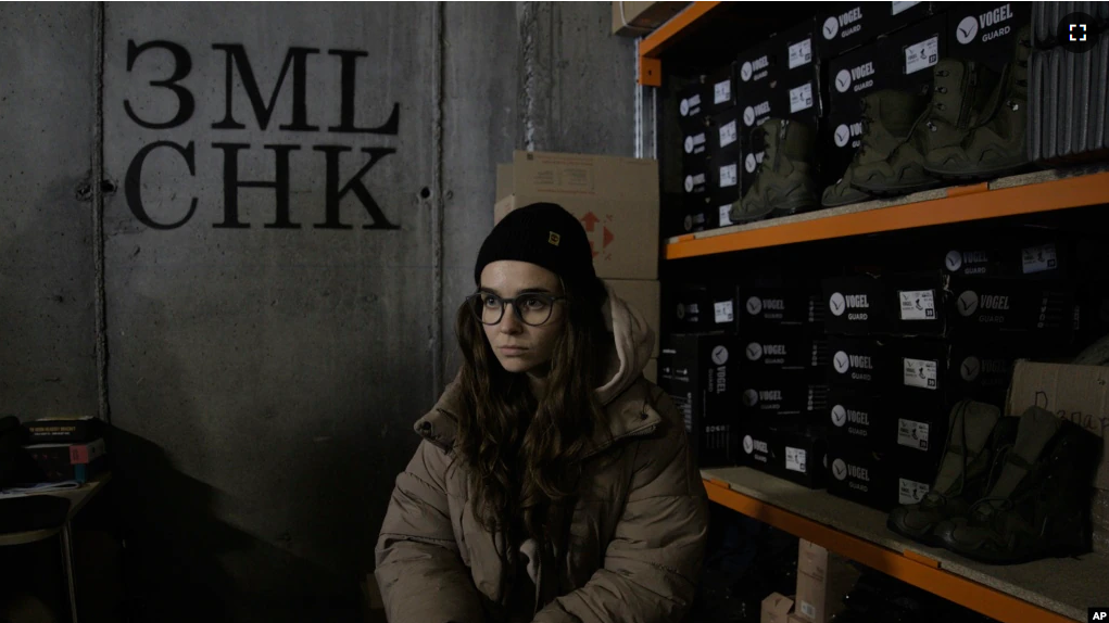 Co-founder Kseniia Drahaniuk of the nonprofit group Zemliachky pauses during an interview in front of shelves stacked with military boots at its supply room in Kyiv, Ukraine, on Tuesday, Dec. 6, 2022. (AP Photo/Vasilisa Stepanenko)