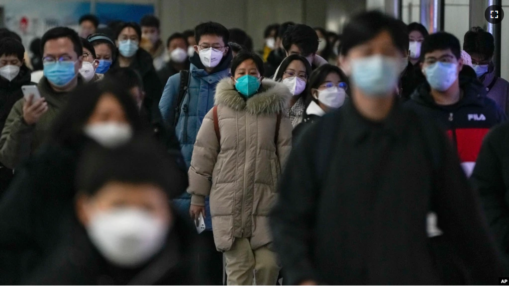 Masked commuters walk through a walkway in between two subway stations as they head to work during the morning rush hour in Beijing, Tuesday, Dec. 20, 2022. (AP Photo/Andy Wong)