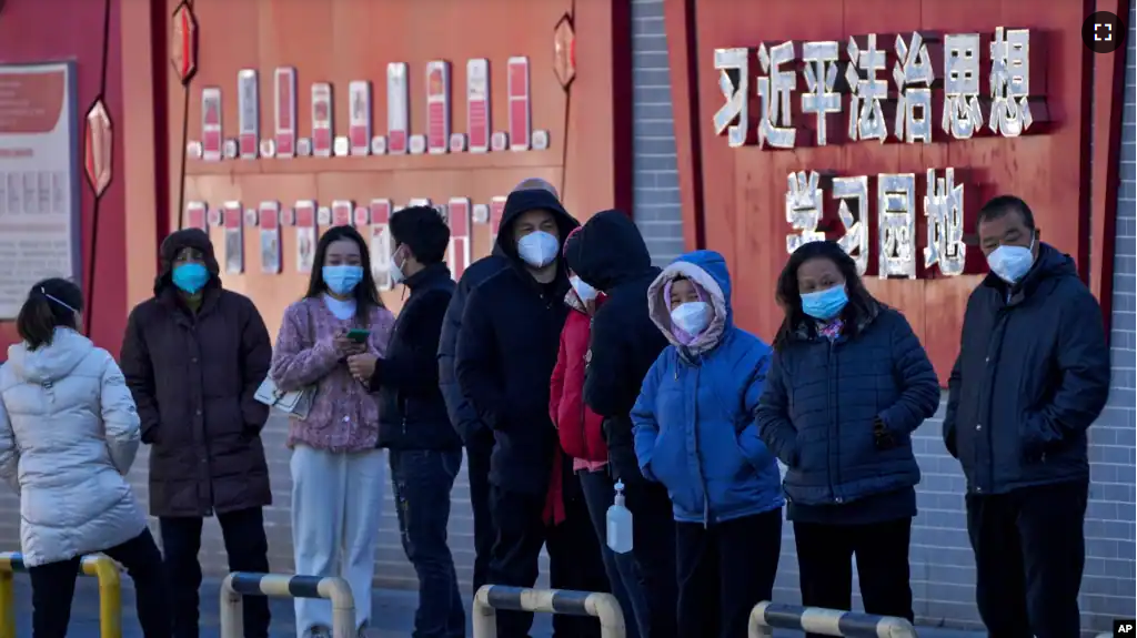 People line up for their COVID-19 tests along a wall displaying the words "Xi Jinping rule of law ideology learning ground" in Beijing, Monday, Dec. 5, 2022. China announced on Dec. 7 that it is easing some of the world's most severe anti-virus controls. (AP Photo/Andy Wong)