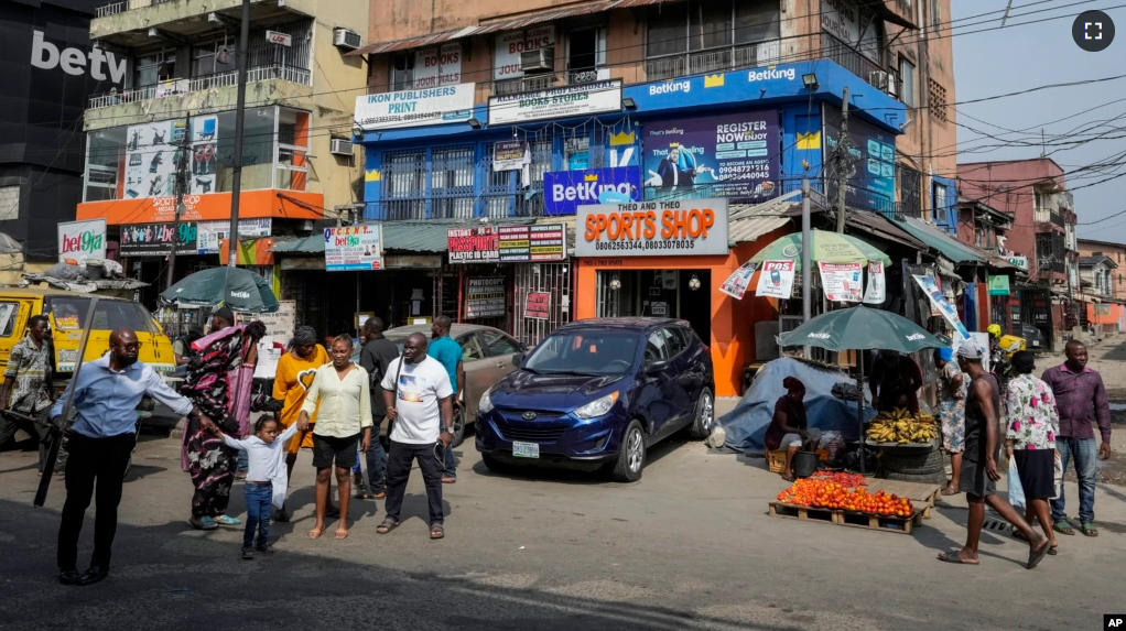 People walk past sports betting shops on a street in Lagos, Nigeria, Monday, Dec. 5, 2022. (AP Photo/Sunday Alamba)