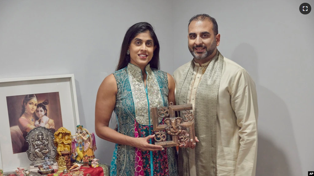 Sheetal Deo and her husband, Sanmeet Deo, hold a Hindu swastika symbol in their home in Syosset, N.Y., on Sunday, Nov. 13, 2022. (AP Photo/Andres Kudacki)