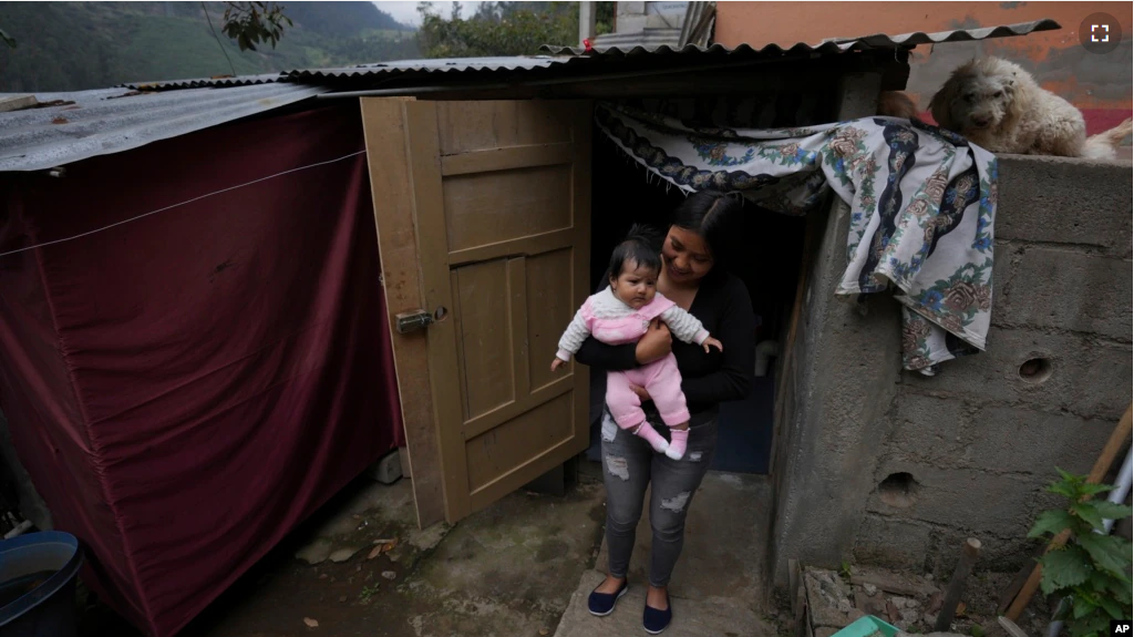 Single mother Katherine Gualotuna holds her four-month-old daughter Arleth outside a one-bedroom shack where they live with Gualotuna's parents in Zámbiza, a rural town northeast of Quito, Ecuador on November 15, 2022. (AP Photo/Dolores Ochoa)