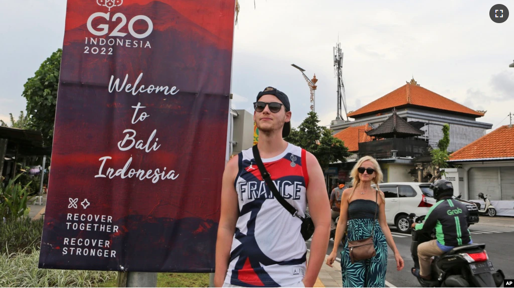 FILE - Tourists walk past a G20 banner in Nusa Dua, Bali, Indonesia on Friday, Nov. 11, 2022. The tropical island's ailing tourism industry returned after a two-year closure due to the pandemic. (AP Photo/Firdia Lisnawati)