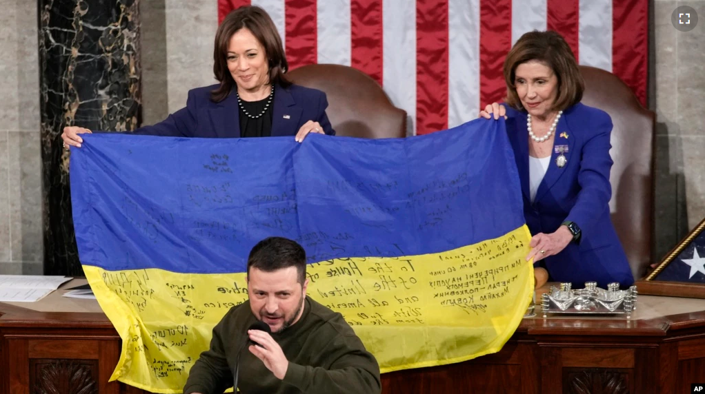 Vice President Kamala Harris and House Speaker Nancy Pelosi of Calif., right, hold a Ukrainian flag autographed by front-line troops in Bakhmut that Ukrainian President Volodymyr Zelenskyy presented to lawmakers in Washington, Wednesday, Dec. 21, 2022. (AP Photo/Carolyn Kaster)