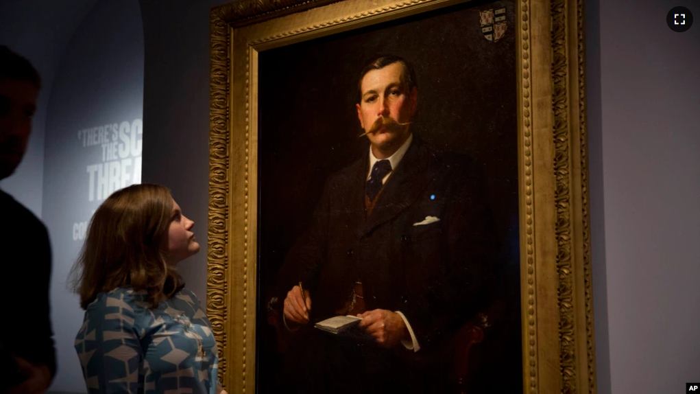 FILE - A Museum of London employee poses for photographers next to an 1897 oil on canvas portrait of Sherlock Holmes at the Museum of London in London, Oct. 16, 2014. (AP Photo/Matt Dunham, File)