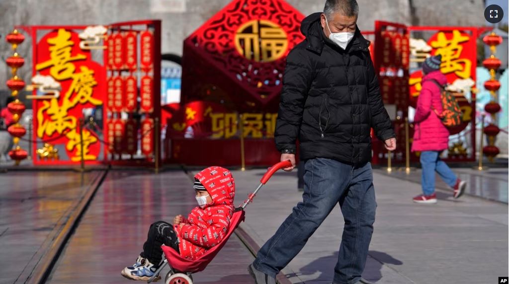 A man pulls a child past a Lunar New Year decoration on display at the Qianmen pedestrian shopping street, a popular tourist spot in Beijing, Jan. 17, 2023. (AP Photo/Andy Wong)