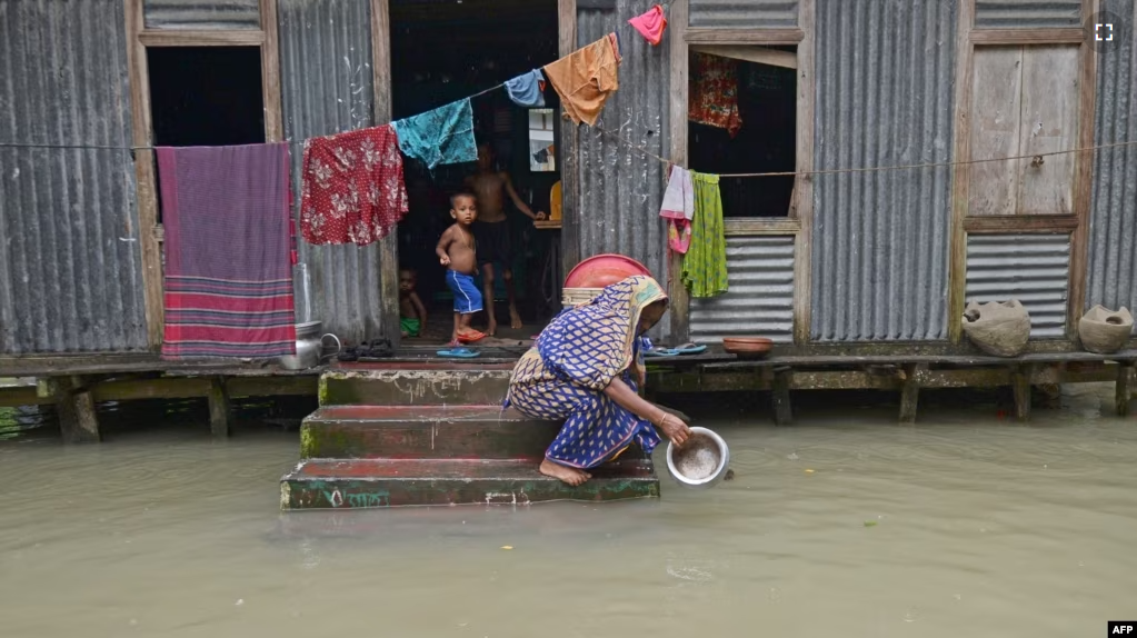 FILE - A woman washes her cooking pot in the flood waters outside her house in Sreenagar on July 20, 2020. (Photo by Munir Uz zaman / AFP)