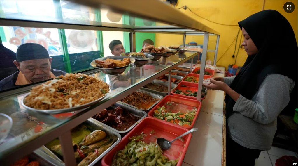 A worker serves customers at a food stall in Bekasi, on the outskirts of Jakarta, Indonesia, Thursday, Feb 2, 2023. (AP Photo/Achmad Ibrahim)