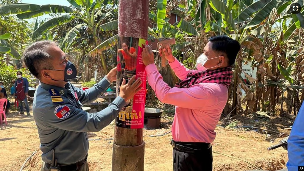 An animal health officer and a military police officer place posters about awareness of H5N1 virus threats in Prey Veng eastern province Cambodia, Thursday, Feb. 23, 2023. (Cambodia Ministry of Health via AP)