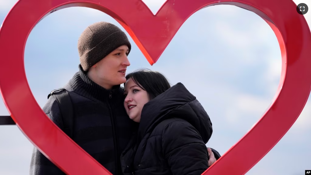 Mariia Vyhivska, from Ukraine, left, and Iurii Kurochkin, from Russia, pose with a heart-shaped sign on the banks of the Ada Ciganlija Lake, in Belgrade, Serbia, Sunday, Feb. 5, 2023. (AP Photo/Darko Vojinovic)