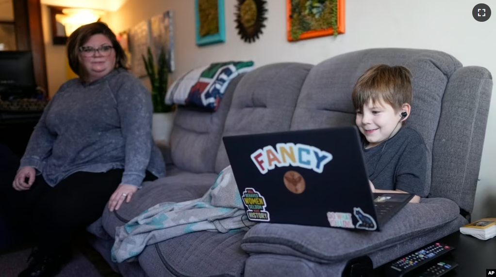 Jessica Blalack, left, watches as her son Phoenix Blalack, 6 , works with a tutor on his laptop in his Indianapolis home, Tuesday, March 7, 2023. (AP Photo/AJ Mast)