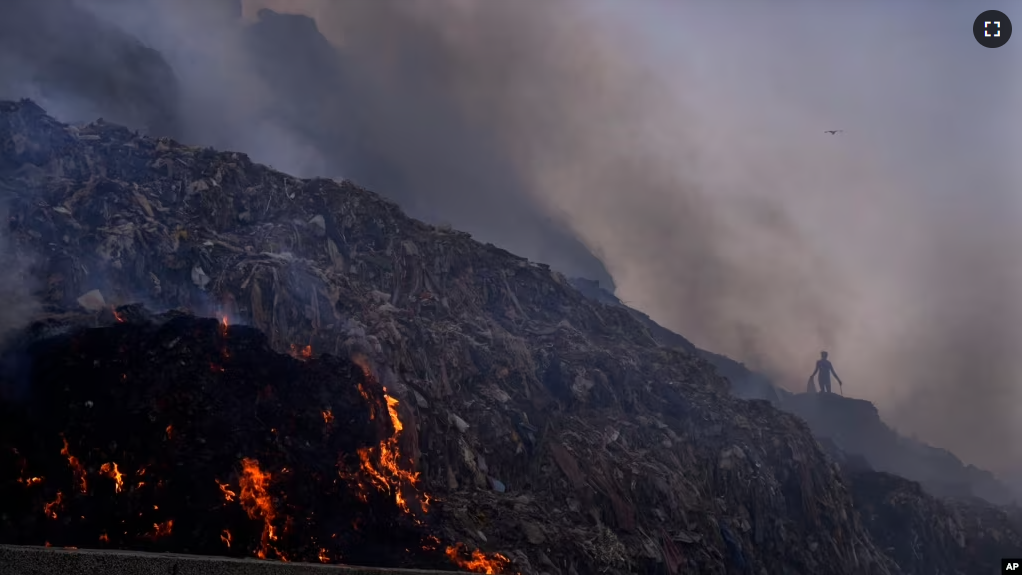 FILE - A person picks through trash for reusable items as a fire rages at the Bhalswa landfill in New Delhi, April 27, 2022. (AP Photo/Manish Swarup, File)