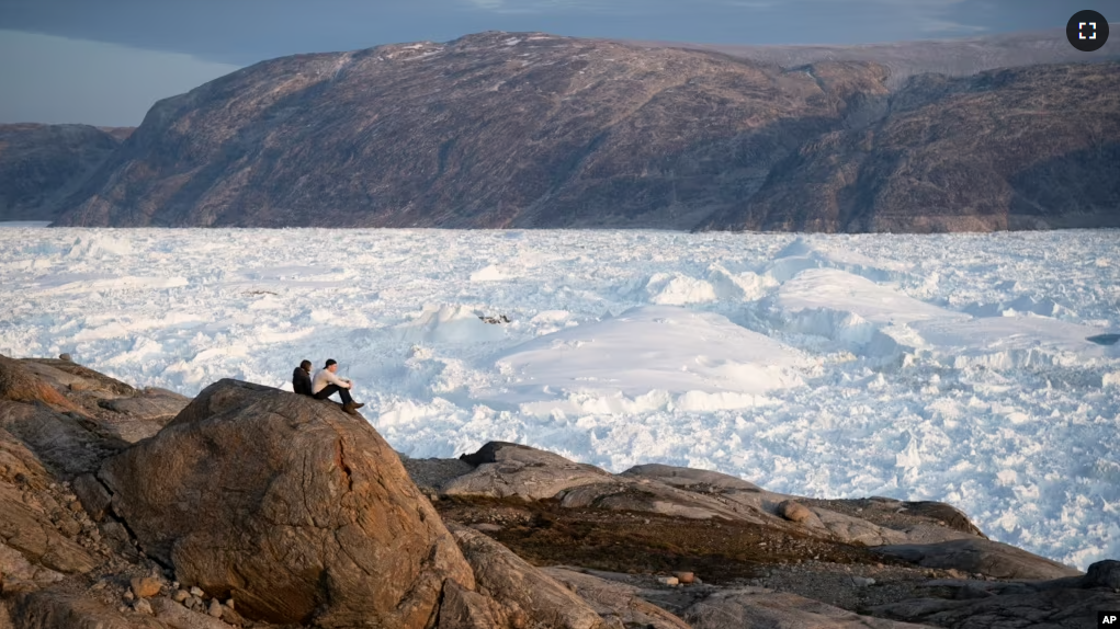 FILE - In this Aug. 16, 2019 photo, NYU student researchers sit on top of a rock overlooking the Helheim glacier in Greenland.(AP Photo/Felipe Dana)