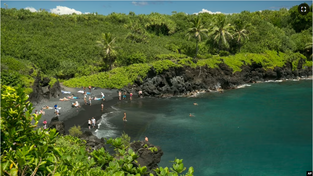 People spend time on the black sand beach at Waianapanapa State Park in Hana, Hawaii, on Sept. 24, 2014. (AP Photo/Marco Garcia, File)