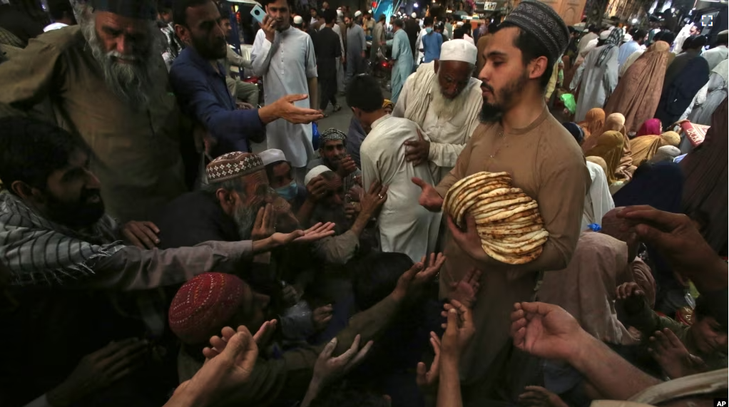 A worker distributes free traditional roti or bread among needy people at a restaurant, in Peshawar, Pakistan on April 16, 2023. (AP Photo/Muhammad Sajjad)