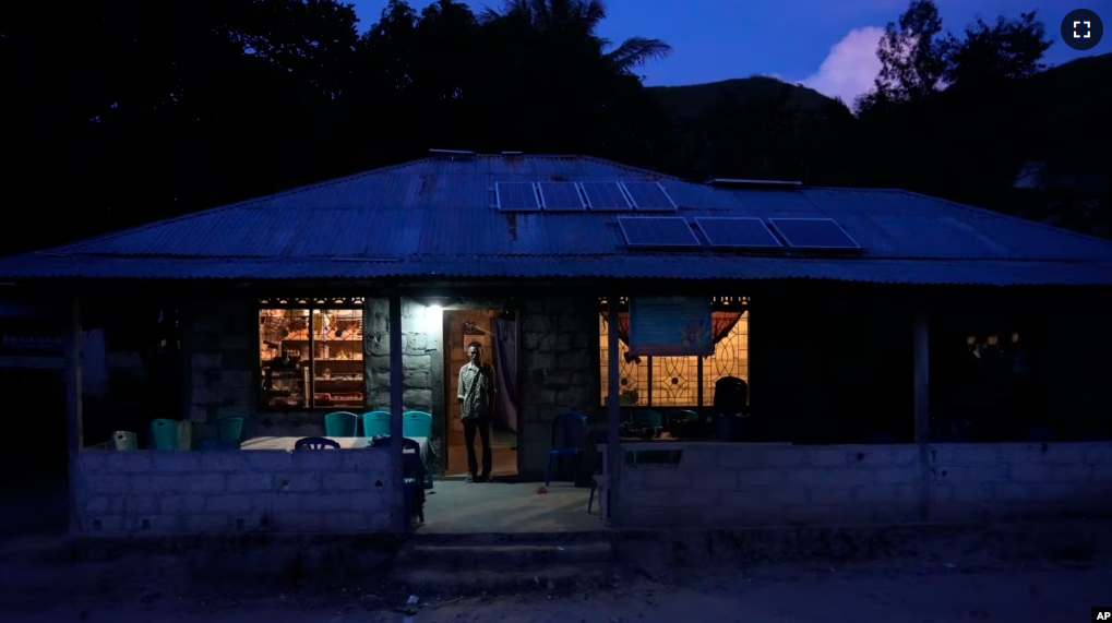 Bara Kilimandang stands at the door of his house whose electricity comes from solar energy in Walatungga on Sumba Island, Indonesia, Tuesday, March 21, 2023. (AP Photo/Dita Alangkara)