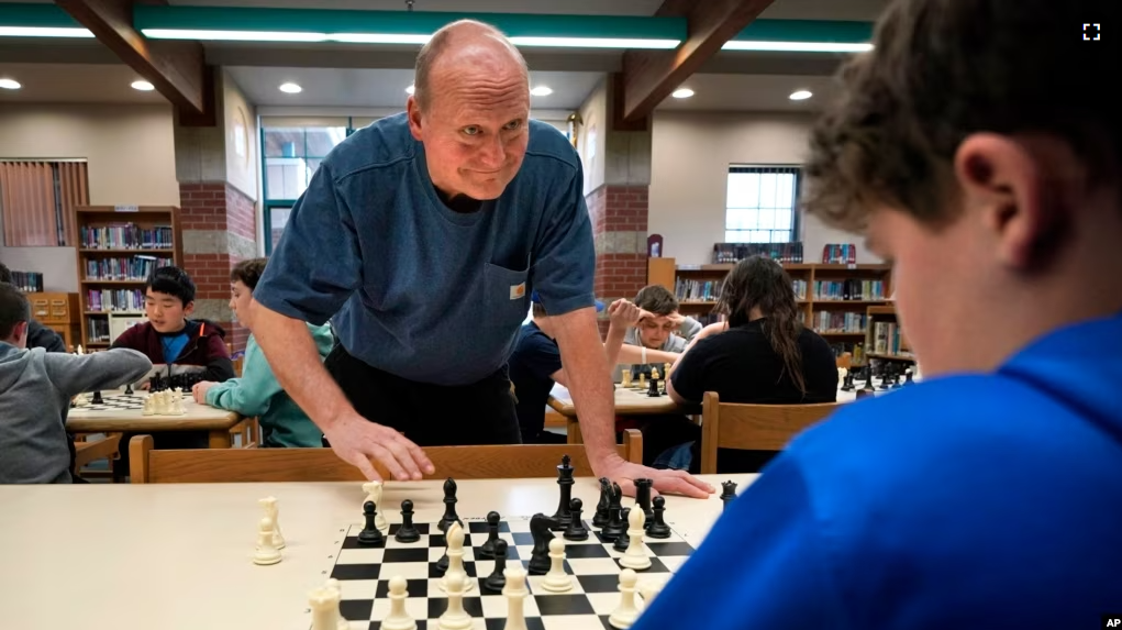 Custodian and chess coach David Bishop challenges 6th-grader Owen Isenhour during after-school practice, Tuesday, April 25, 2023, in Hampden, Maine. Under Bishop's tutelage, the Reeds Brook Middle School chess team has gained national recognition. (AP Photo/Robert F. Bukaty)