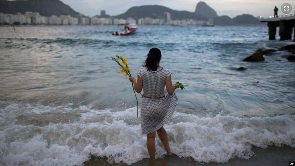 FILE - Many cultures have good luck charms or activities. In this photo, a woman offers flowers to Yemanja, goddess of the sea, for good luck in the coming year during New Year's Eve festivities on Copacabana beach in Rio de Janeiro, Brazil, Dec. 31, 2016. (AP Photo/Leo Correa)