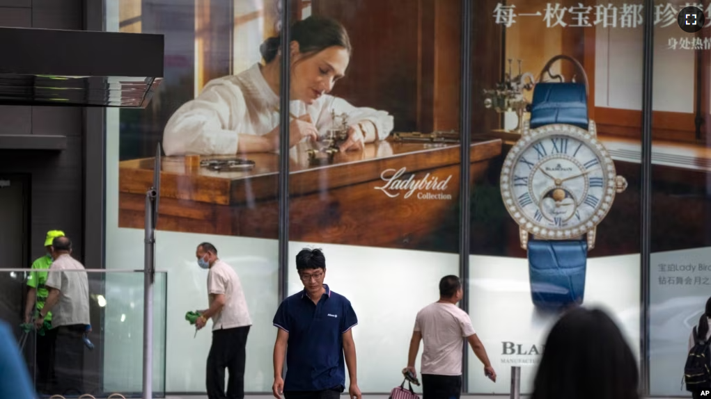 People walk past a billboard for Swiss luxury watch retailer Blancpain at an upscale shopping mall in Beijing, on June 13, 2023. (AP Photo/Mark Schiefelbein)