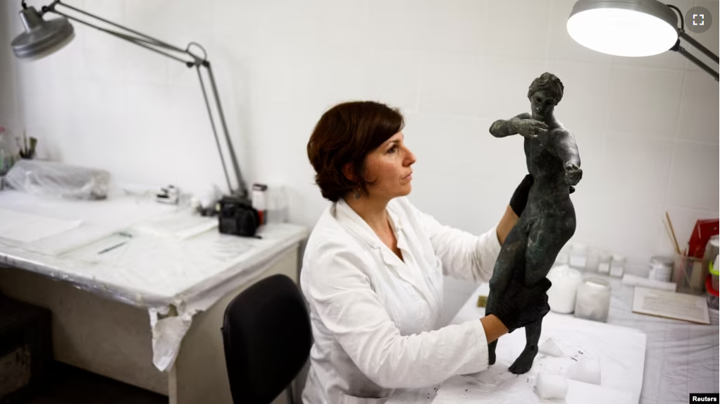 FILE - Restorer Laura Rivaroli works on a bronze statue of Apollo in the pose of an archer. It was discovered in the muddy ruins of an ancient spa in San Casciano dei Bagni, a hilltop village in southern Tuscany. May 29, 2023. (REUTERS/Guglielmo Mangiapane)