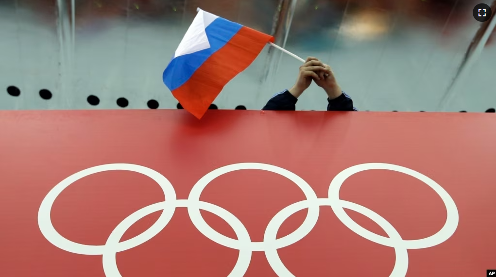 FILE - A Russian flag is held above the Olympic Rings at Adler Arena Skating Center during the Winter Olympics in Sochi, Russia on Feb. 18, 2014. (AP Photo/David J. Phillip, File)