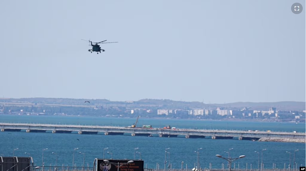 A Russian military helicopter flies over damaged parts of an automobile link of the Crimean Bridge connecting the Russian mainland and the Crimean peninsula over the Kerch Strait on July 17, 2023. (AP Photo)