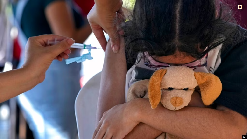 FILE - A girl hugs her stuffed toy as she gets a shot of the Pfizer COVID-19 vaccine at a community health center, in Brasilia, Brazil, Jan. 16, 2022. (AP Photo/Eraldo Peres)