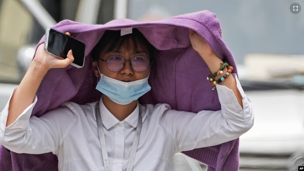 A woman uses a sweater to shield from the sun as she wals on a street on a hot day in Beijing, Monday, July 3, 2023. (AP Photo/Andy Wong)