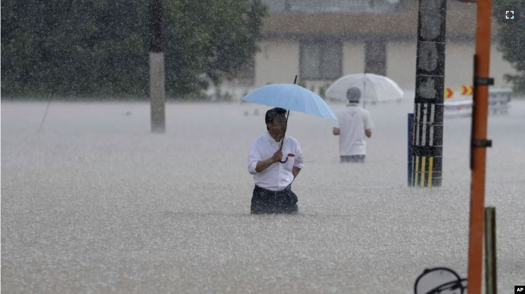 People wade through a street due to a heavy rain in Kurume, Fukuoka prefecture, southern Japan Monday, July 10, 2023.(Kyodo News via AP)