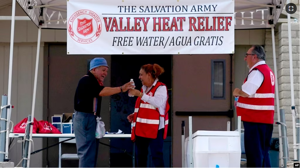 Salvation Army volunteer Francisca Corral, center, gives water to a man at a their Valley Heat Relief Station, Tuesday, July 11, 2023 in Phoenix. (AP Photo/Matt York)