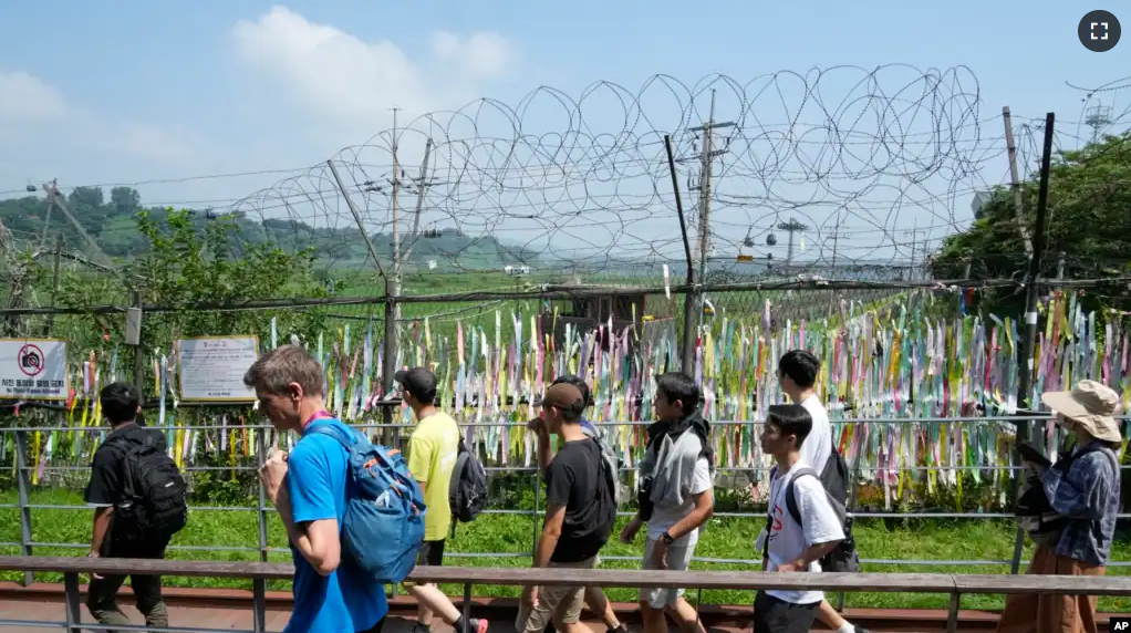 Visitors pass by a wire fence decorated with ribbons written with messages wishing for the reunification of the two Koreas at the Imjingak Pavilion in Paju, South Korea, near the border with North Korea, Wednesday, July 19, 2023.(AP Photo/Ahn Young-joon)