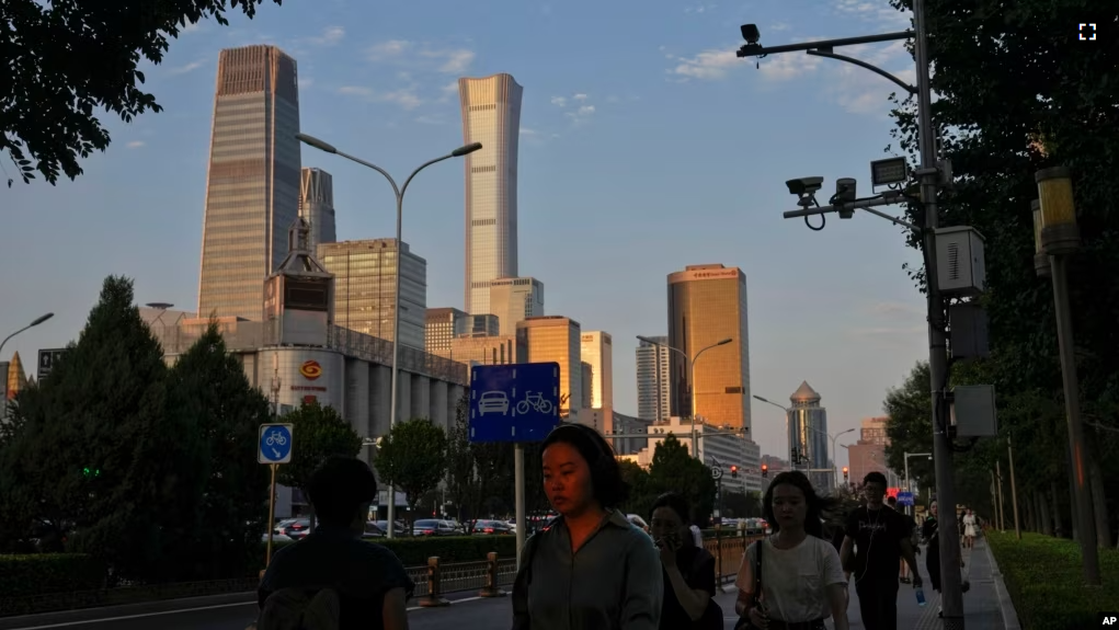 An evening sunlight casts on a woman as people walk near the Central Business District during the rush hour in Beijing on Monday, Aug. 14, 2023. (AP Photo/Andy Wong)