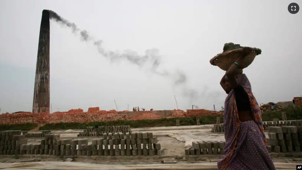 FILE - Smoke emits from chimney as a Bangladeshi female worker carries clay at a brick field at Amin Bazar, outskirts of Dhaka, Bangladesh, Thursday, May 14, 2009. (AP Photo/ Pavel Rahman/File)