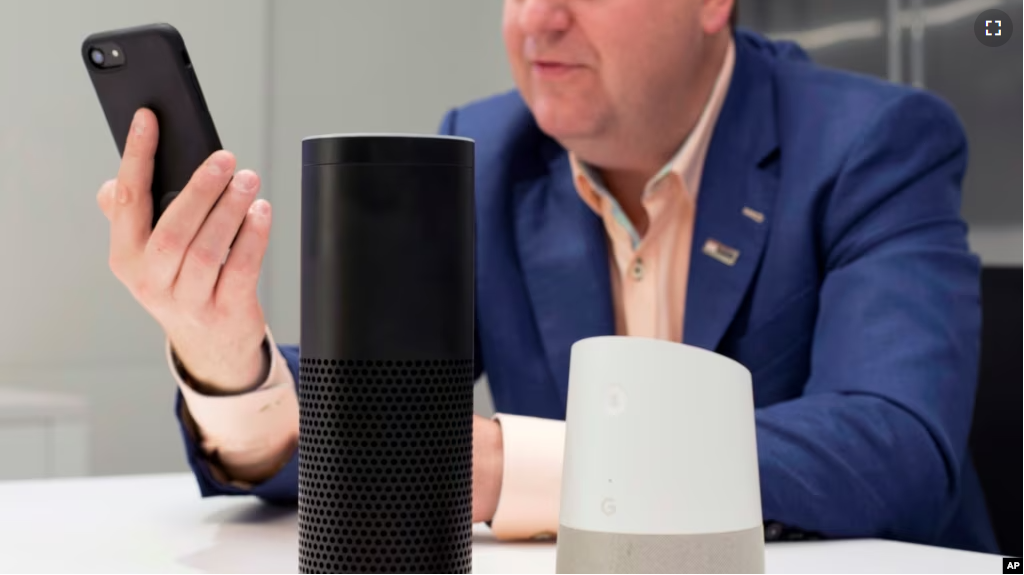 A man holds an iPhone next to an Amazon Echo, center, and a Google Home, right, in New York on June 14, 2018. (AP Photo/Mark Lennihan)