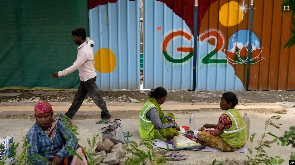 Laborers take a lunch break near a construction site covered with G20 summit logo in New Delhi, India, Thursday, Aug. 24, 2023. (AP Photo/Manish Swarup)