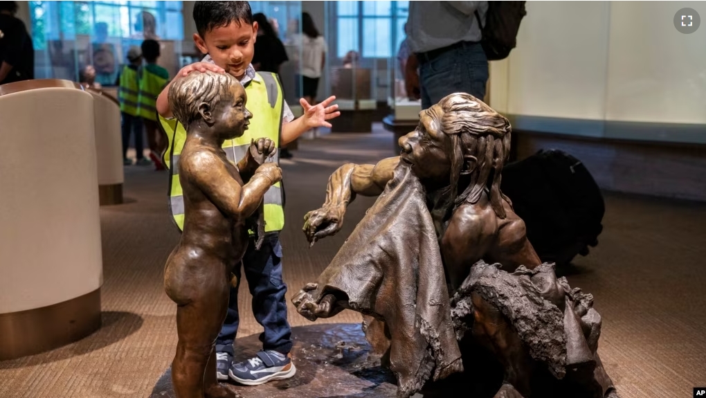 FILE - A boy pats the head of a sculpture of a Neanderthal boy, inside the Smithsonian Hall of Human Origins, Thursday, July 20, 2023, at the Smithsonian Museum of Natural History in Washington.(AP Photo/Jacquelyn Martin)