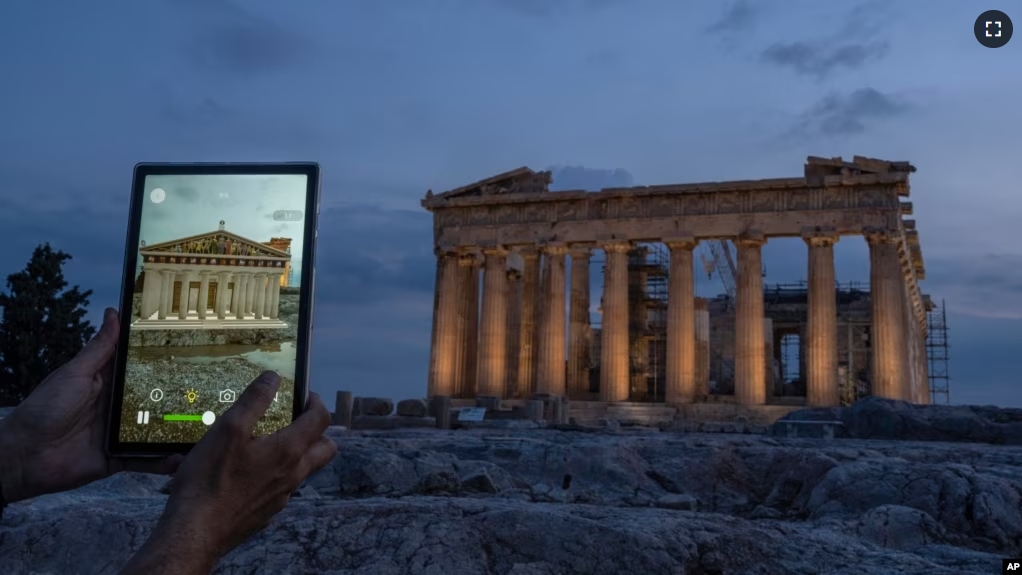 A man holds up a tablet showing a digitally overlayed virtual reconstruction of the ancient Parthenon temple, at the Acropolis Hill in Athens, Greece on Tuesday, June 13, 2023. (AP Photo/Petros Giannakouris)