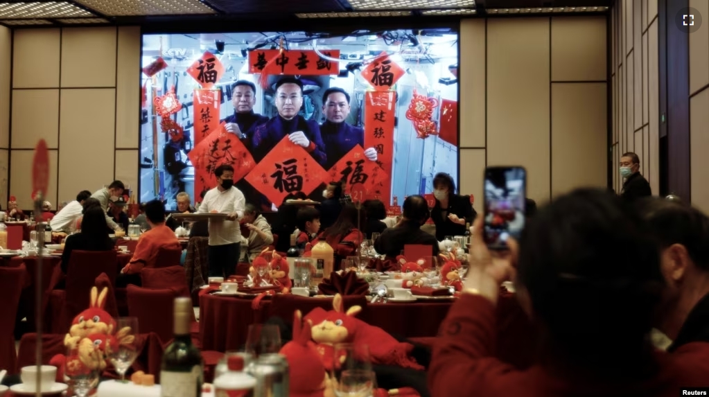 FILE - A woman takes pictures of a screen displaying the Spring Festival greetings by Chinese astronauts Fei Junlong, Deng Qingming and Zhang Lu from China's space station, during a Lunar New Year's Eve dinner in Beijing, China, January 21, 2023. (REUTERS/Florence Lo)