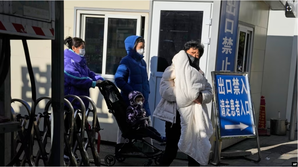 A woman carries a child as they leave a children's hospital in Beijing, Friday, Nov. 24, 2023. (AP Photo/Ng Han Guan)