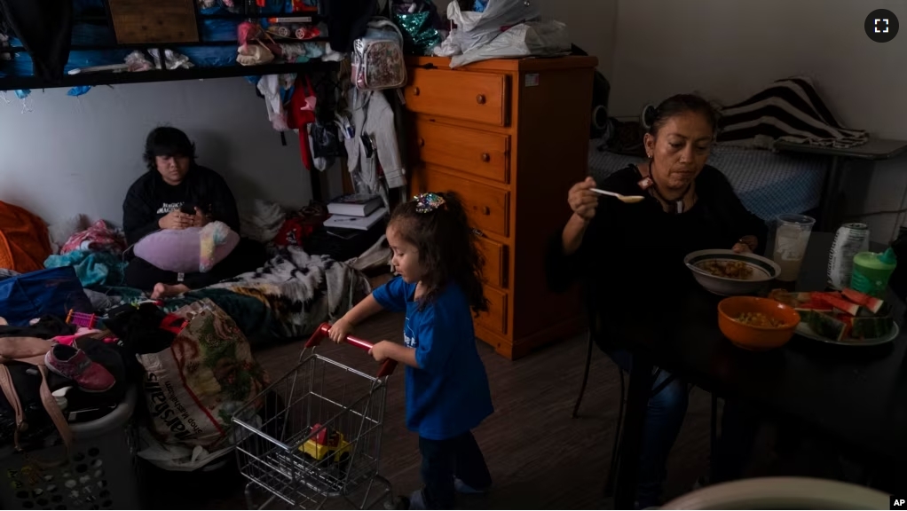 Deneffy Sánchez, left, looks at his smartphone on a bunk bed he shares with his mother, Lilian Lopez, right, and sister, Jennifer, in a shared studio apartment in Los Angeles, Saturday, Sept. 9, 2023. (AP Photo/Jae C. Hong)