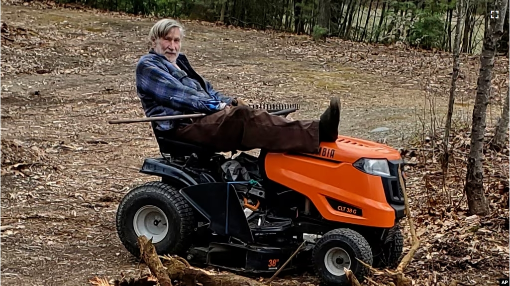 In this photo provided by Ed Smith, Geoffrey Holt rests his leg on top of his riding mower in Hinsdale, N.H., on April 4, 2020. Holt left the town of Hinsdale nearly $4 million when he died last June. (Ed Smith via AP)