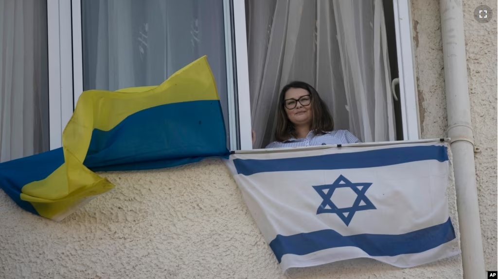 Tatyana Prima, who fled Mariupol, Ukraine, poses for a portrait with her national flag and the Israeli flag she displays outside of her apartment window in Ashkelon, southern Israel, Wednesday, Nov. 8, 2023. (AP Photo/Maya Alleruzzo)