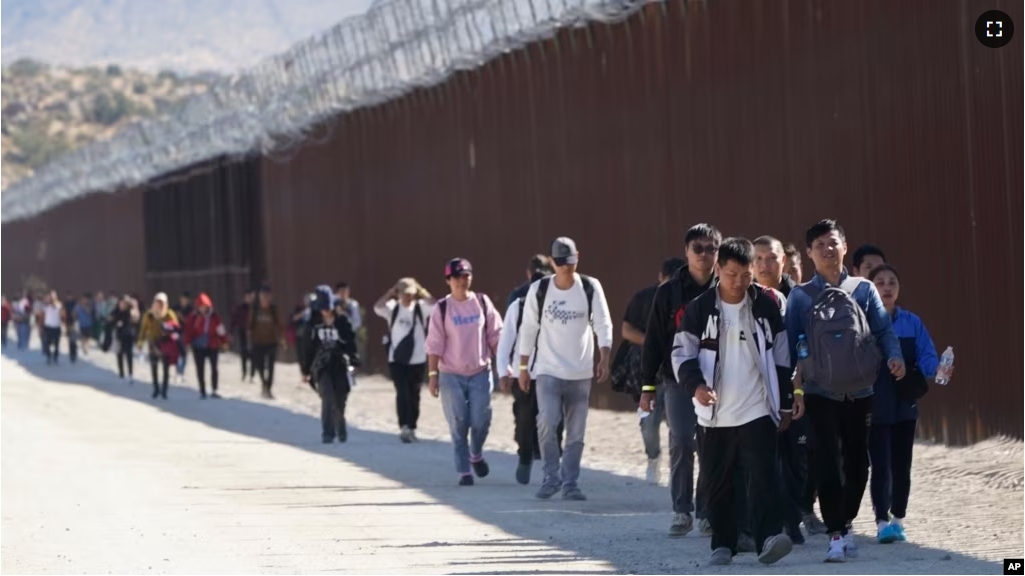 A group of people, including many from China, walk along the wall after crossing the border with Mexico to seek asylum, Tuesday, Oct. 24, 2023, near Jacumba, California. (AP Photo/Gregory Bull)