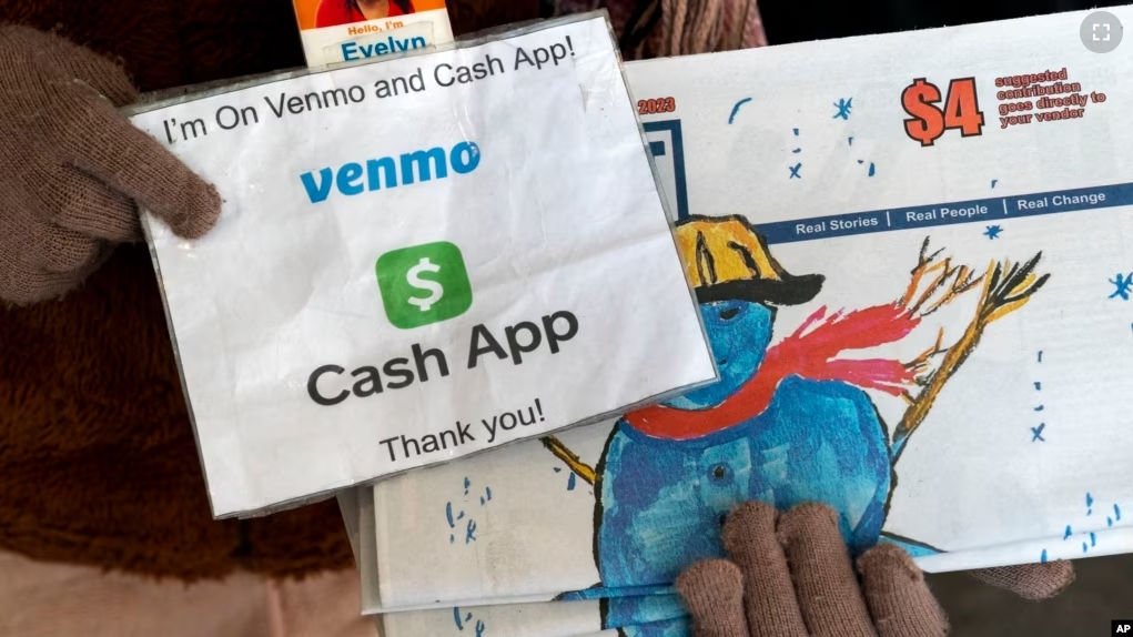 A vendor selling Street Sense holds up her sign saying she can accept donations from cashless apps like Venmo and CashApp, Wednesday, Dec. 6, 2023, in Washington. (AP Photo/Jacquelyn Martin)