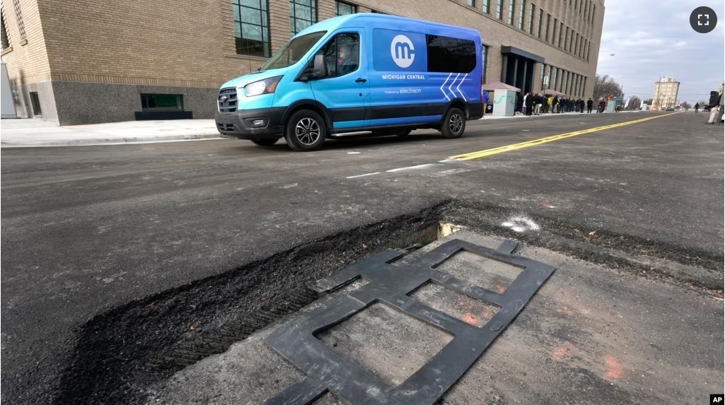 An electric van drives past a visible in-road wireless charging coil to be installed in a street in Detroit, Wednesday, Nov. 29, 2023. (AP Photo/Paul Sancya)