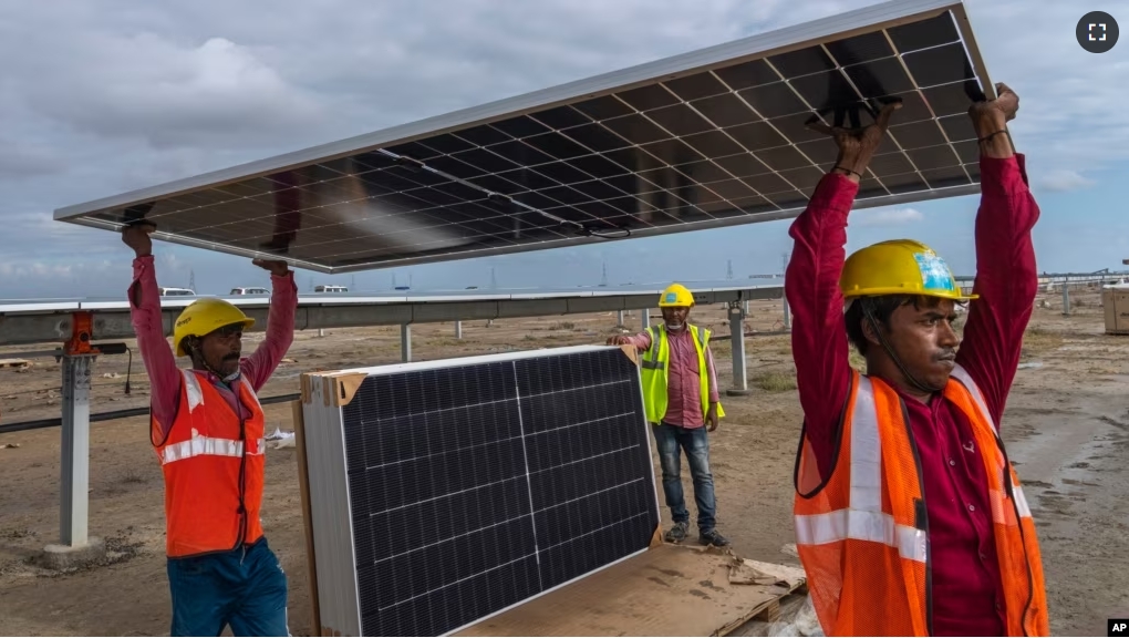 Workers carry a solar panel for installation at the under-construction Adani Green Energy Limited's Renewable Energy Park in the salt desert of Karim Shahi village. (AP Photo/Rafiq Maqbool)