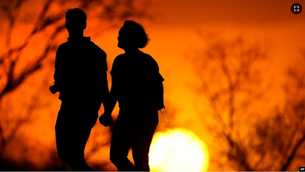 In this file photo, a couple walks through a park at sunset, March 10, 2021, in Kansas City, Mo. (AP Photo/Charlie Riedel, File)